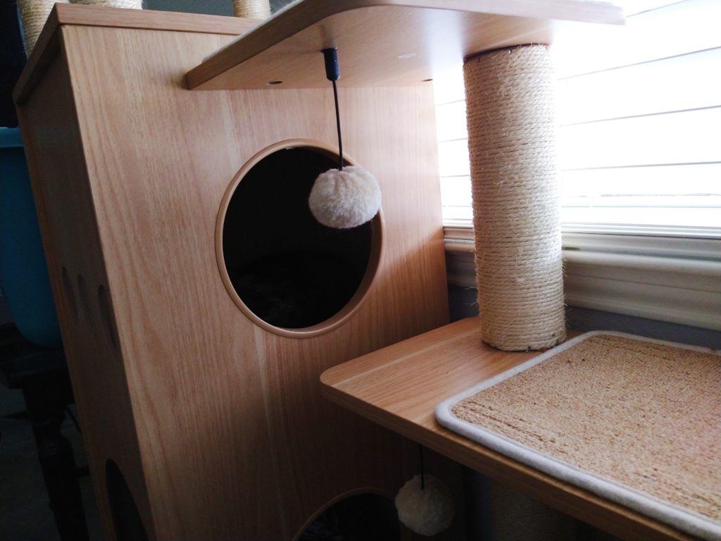 Wooden scratching post with a cubby inside and steps, with a tortie cat sleeping inside
